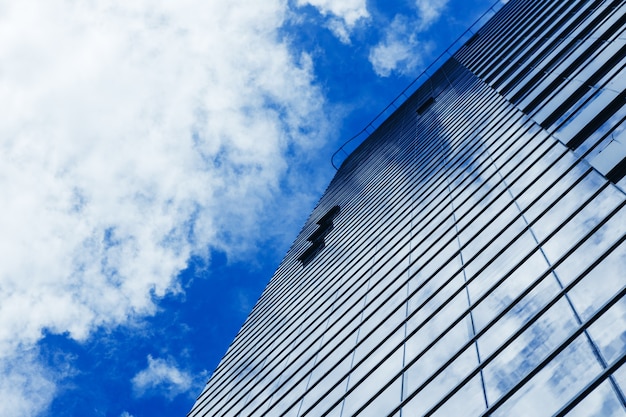 Glazen wolkenkrabber gebouw met bewolkte blauwe hemelachtergrond