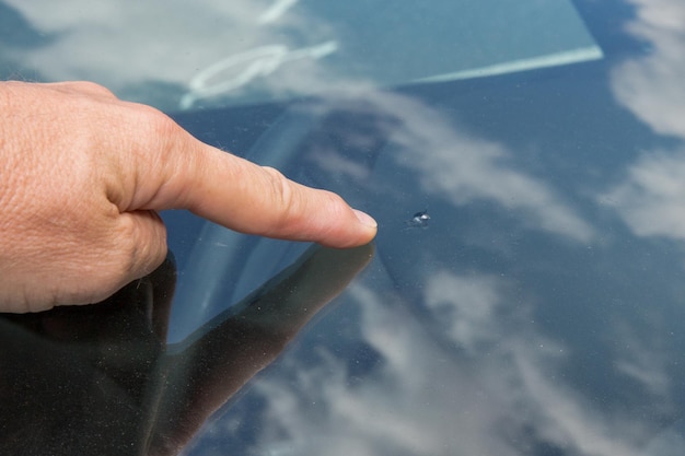 ガラス屋のフロントガラスの男性の指は、壊れた車のフロントガラスへの衝撃を示しています