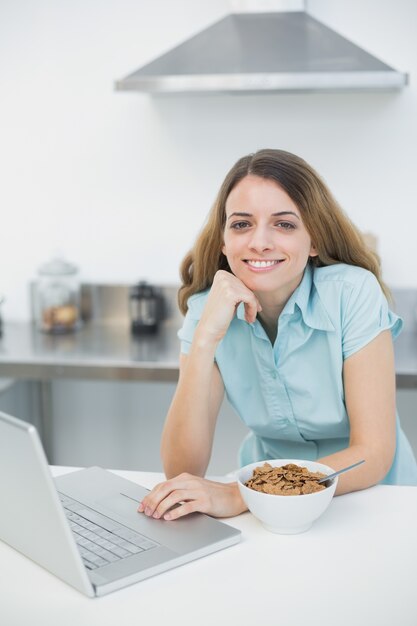 Gleeful woman using her laptop smiling at camera