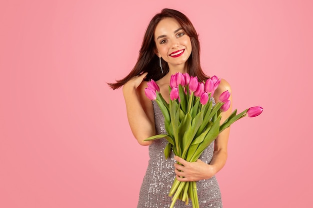 Gleeful young woman with lustrous hair holding a lush bouquet of pink tulips