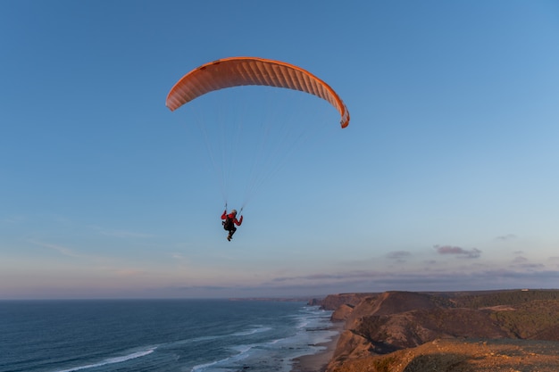 Glijscherm dat over de kust bij zonsondergang vliegt. Paragliding sport