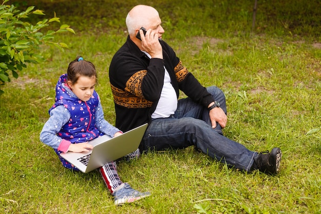 Glimlach aantrekkelijke stijlvolle grootvader met smartphone, kleindochter met laptop. met behulp van internet sociale media netwerktechnologie met digitaal horloge