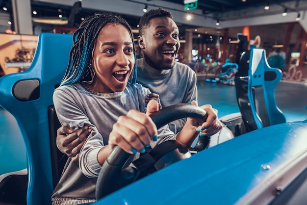 Glimlach Afrikaans Amerikaans meisje die blauwe auto in arcade berijden.