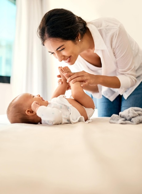 Glimlach liefde en een moeder met haar baby in de slaapkamer van hun huis samen voor een speelse band Gezinskinderen en een gelukkige jonge mama brengen tijd door met haar pasgeboren baby op bed voor de lol of vreugde