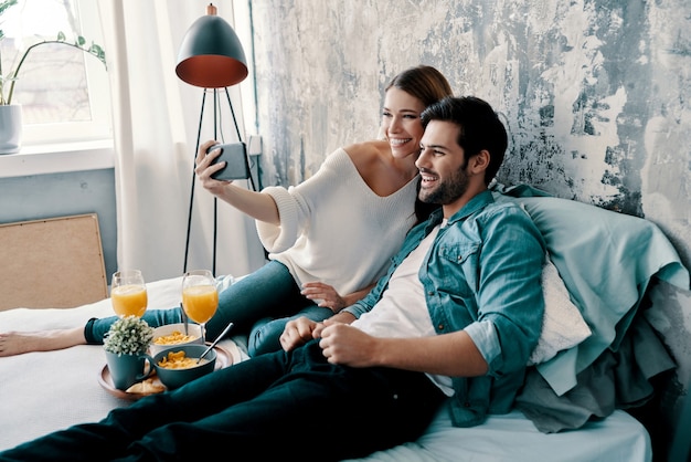 Glimlach! mooi jong stel dat selfie maakt en glimlacht terwijl ze thuis tijd in bed doorbrengt