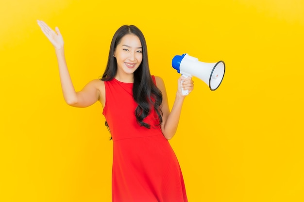 Glimlach van de portret de mooie jonge aziatische vrouw met megafoon op gele muur