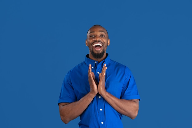 Glimlachen, lachen. Zwart-wit portret van jonge Afro-Amerikaanse man geïsoleerd op blauwe studio muur.