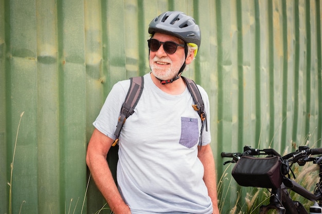 Glimlachend aantrekkelijke senior man met helm en rugzak genieten van sportactiviteit met elektrische fiets in openlucht groene achtergrond