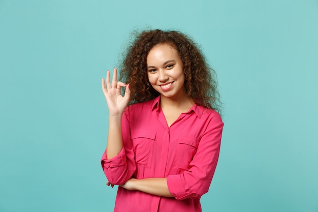 Glimlachend Afrikaans Amerikaans meisje in casual kleding met OK gebaar, op zoek naar camera geïsoleerd op blauwe turquoise muur achtergrond in studio. Mensen oprechte emoties, lifestyle concept. Bespotten kopie ruimte.