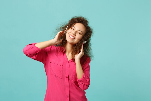 Glimlachend Afrikaans meisje in vrijetijdskleding die de ogen gesloten houdt, muziek luistert met een koptelefoon geïsoleerd op een blauwe turquoise muurachtergrond. Mensen oprechte emoties, lifestyle concept. Bespotten kopie ruimte.