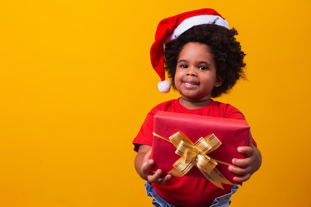 Glimlachend afro kind in de rode hoed van de Kerstman met kerstcadeau in de hand. Kerstconcept.