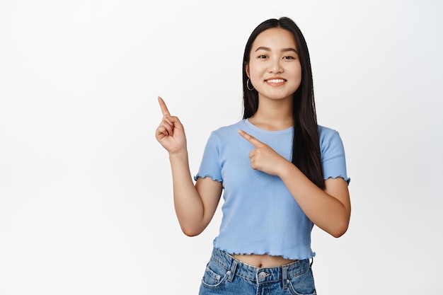 Glimlachend Aziatisch meisje dat naar links wijst en een verkoopbanner toont die een promo-aanbieding aankondigt die in een t-shirt op een witte achtergrond staat