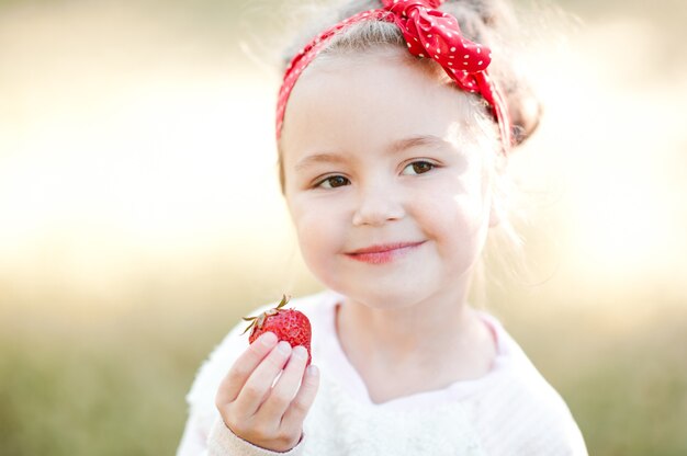 Foto glimlachend babymeisje dat verse aardbeien in de buitenlucht eet