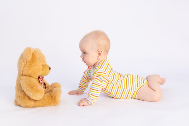 Glimlachend babymeisje ligt op wit geïsoleerd in een lichte Romper voor een zachte teddybeer