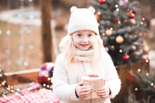 Glimlachend babymeisje met kerstdoos boven de kerstboom buiten