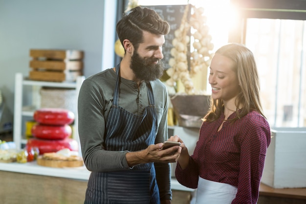 Glimlachend bakkerijpersoneel die mobiele telefoon met behulp van bij teller