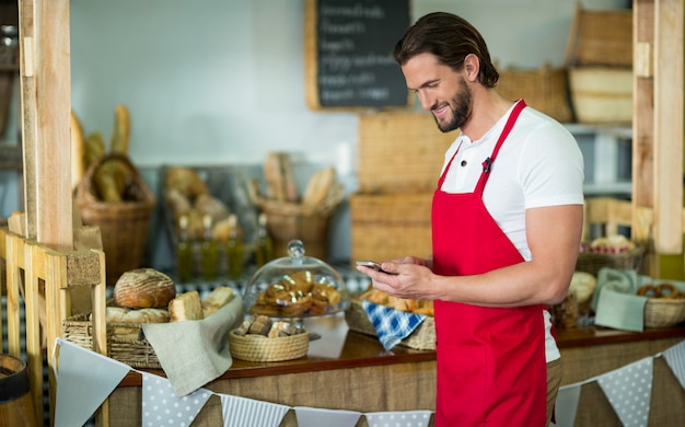 Glimlachend bakkerijpersoneel met behulp van mobiele telefoon aan balie