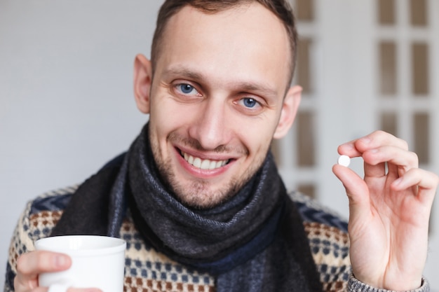 Glimlachend betrapt toont een koude man pillen voor gezondheid alvorens te nemen