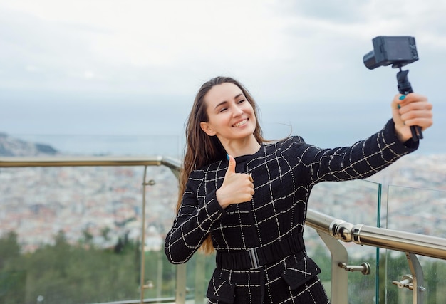 Glimlachend bloggermeisje neemt selfie door gebaar van perfect te tonen tegen de achtergrond van uitzicht op de stad