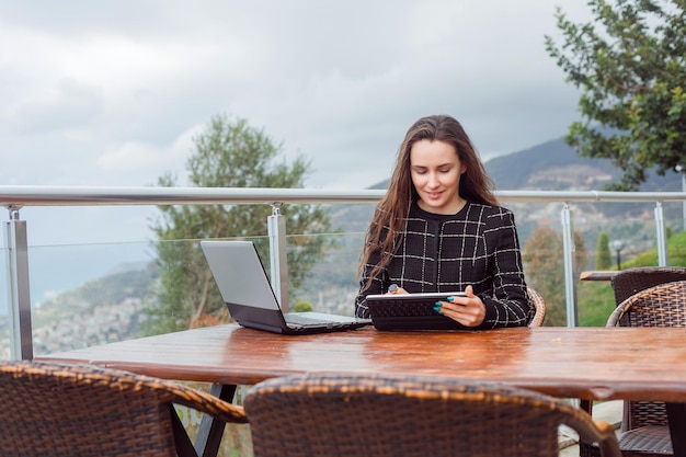 Glimlachend bloggermeisje werkt aan laptop door op de achtergrond van de natuurweergave te zitten