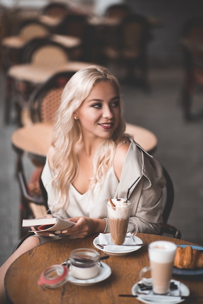 Glimlachend blond meisje dat koffie drinkt en plezier heeft in café