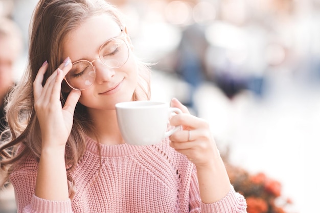 Glimlachend blond meisje met kopje thee met ogen dicht in café