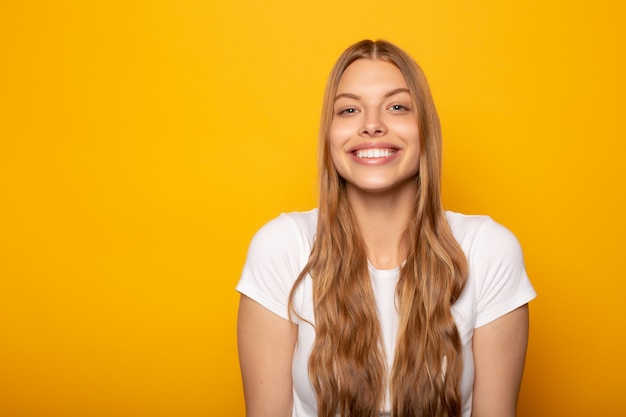 glimlachend blond meisje met lang haar dat op geel wordt geïsoleerd