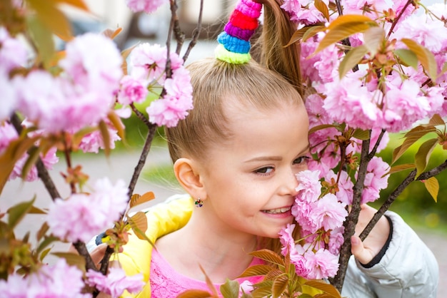 Glimlachend blond meisje permanent in een bloeiende tuin Bloeiende kers portret van mooi meisje Close up van kleine model gezicht Sakura bloeiende lentetijd