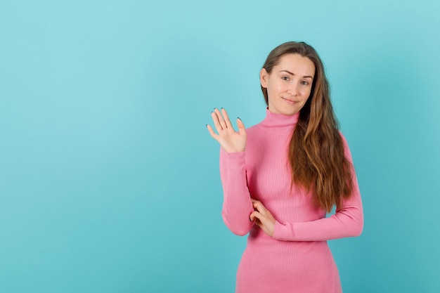 Glimlachend blond meisje toont hallo gebaar door hand op te steken op blauwe achtergrond