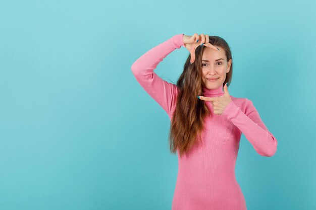 Glimlachend blond meisje vertoont framegebaar met handen op blauwe achtergrond