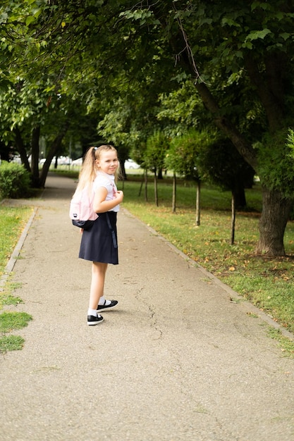 Foto glimlachend blond schoolmeisje in schooluniform met roze rugzak die buiten naar school gaat