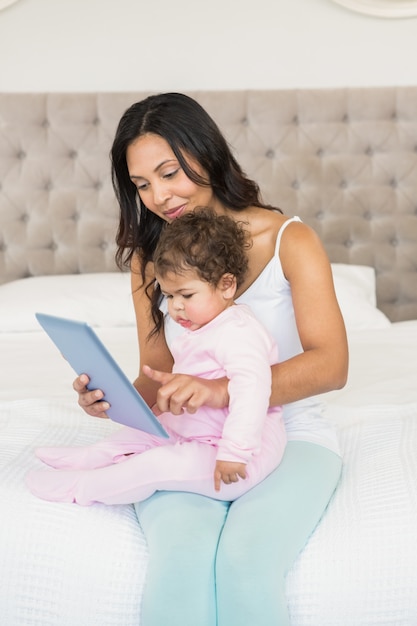 Glimlachend brunette die haar baby houden en tablet in slaapkamer gebruiken