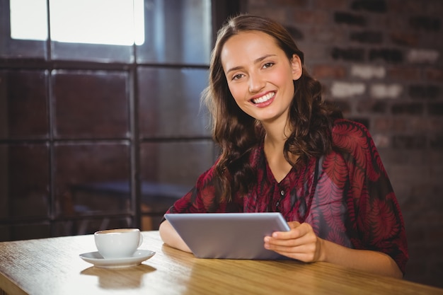 Glimlachend brunette die koffie hebben en tablet houden