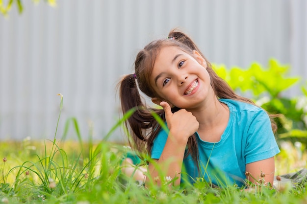 Glimlachend brunette meisje met twee staarten ligt op het groene gras in de zomertuin