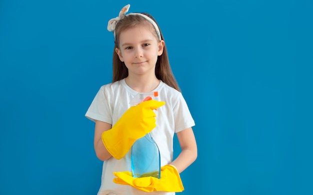 Glimlachend charmant klein huisvrouwenmeisje in gele handschoenen voor het wassen, huiswerk maken geïsoleerd op een blauwe achtergrond het concept van huishoudelijke managers