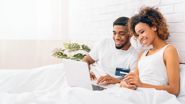Glimlachend echtpaar met een laptop in bed thuis