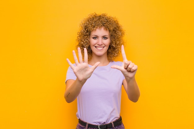 Glimlachend en vriendelijk kijkend, met nummer zeven of zevende met de hand naar voren, aftellend