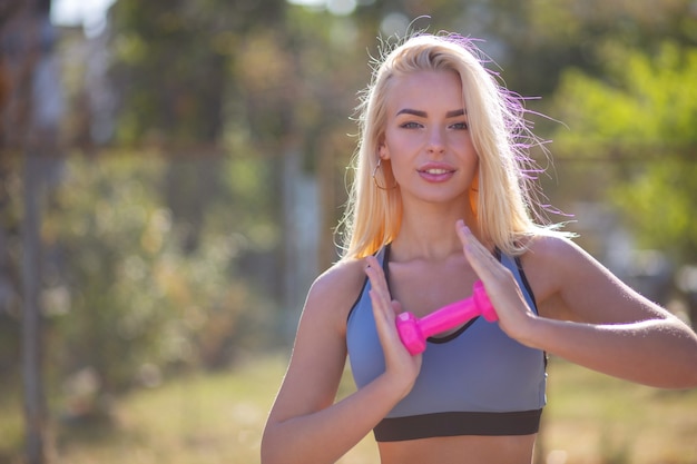 Glimlachend fit blonde vrouw poseren met halters in het stadion. Ruimte voor tekst