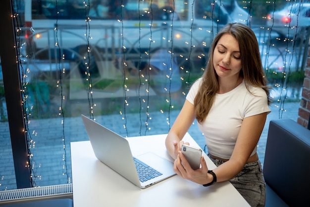 Glimlachend freelance meisje dat op een laptop in een café werkt en videogesprekken voert of telefoneert, de werkdag van een gratis jonge vrouw of student