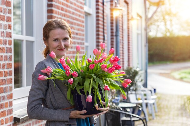 Glimlachend gelukkig meisje met een vaas met roze tulpen in de buurt met een traditioneel nederlands huis. nederland