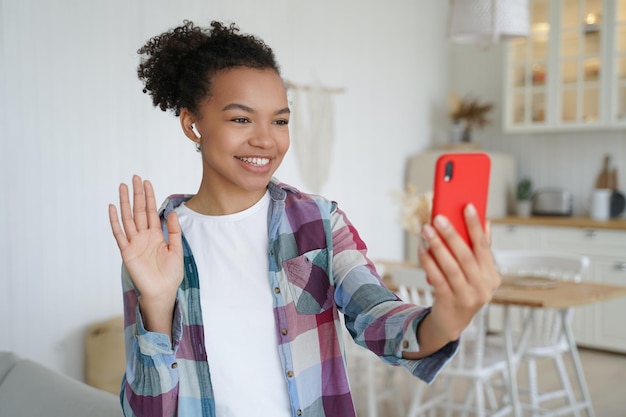 Glimlachend gemengd ras meisje houdt telefoon maakt begroeting gebaar online praten op video-oproep thuis