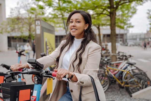 glimlachend gemengd ras vrouw kijken camera rijden op elektrische scooter buitenshuis. Reisconcept