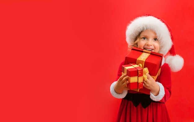 Glimlachend grappig babymeisje die in Santa rode hoed de giften van Kerstmis in hand houden.