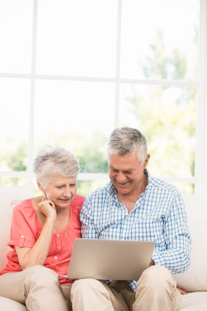 Glimlachend hoger paar die laptop op de bank met behulp van