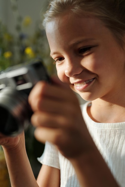 Glimlachend jeugdig meisje met fotocamera die door nieuwe foto's kijkt