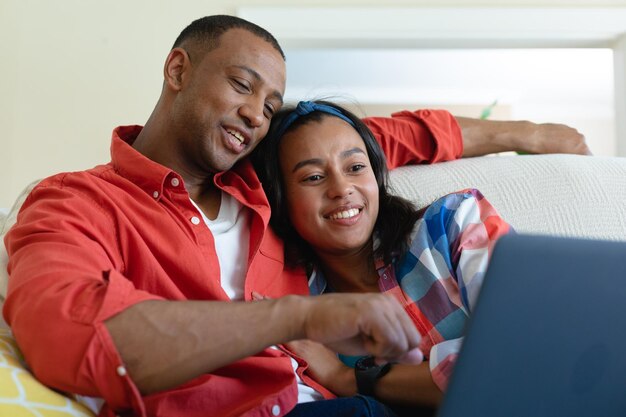 Glimlachend jong Afrikaans Amerikaans echtpaar dat thuis samen naar laptop kijkt. mensen, saamhorigheid en technologieconcept, ongewijzigd.