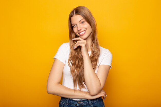 glimlachend jong blondemeisje met lang haar wat betreft kin die op geel wordt geïsoleerd