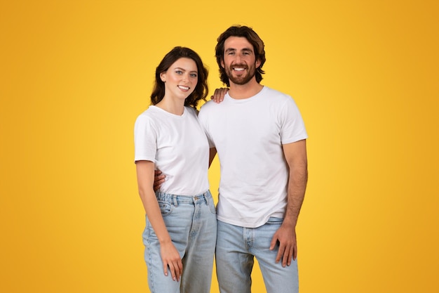 Glimlachend jong echtpaar staat samen in witte T-shirts en blauwe spijkerbroek