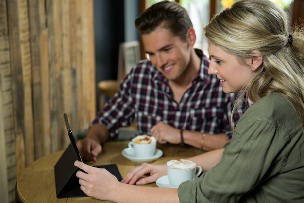 Glimlachend jong koppel met behulp van digitale tablet aan tafel in de coffeeshop