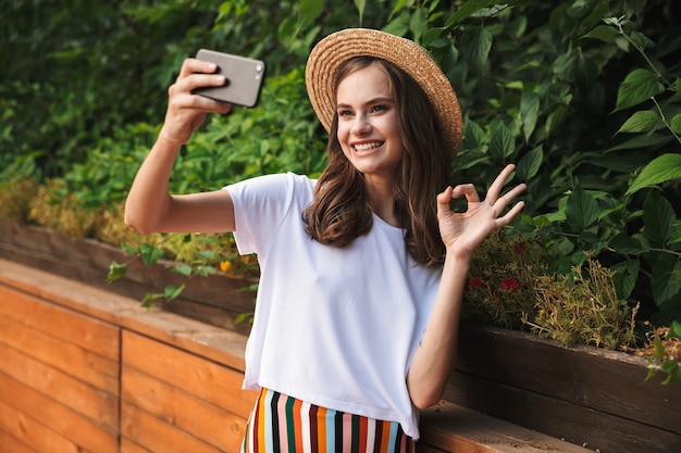 Glimlachend jong meisje dat een selfie met mobiele telefoon neemt in het park buiten